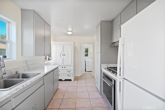 kitchen featuring stainless steel appliances, gray cabinets, washer / clothes dryer, light tile patterned flooring, and sink