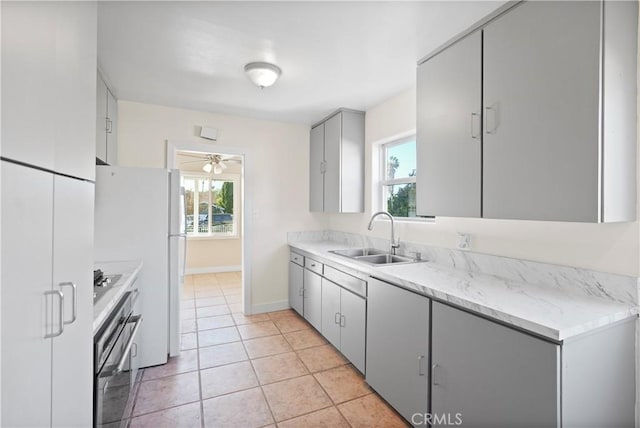 kitchen featuring stainless steel oven, light tile patterned floors, gray cabinetry, ceiling fan, and sink