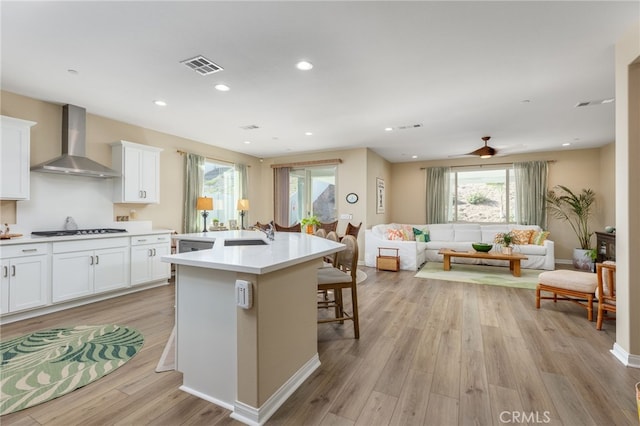 kitchen featuring an island with sink, white cabinetry, a breakfast bar area, and wall chimney exhaust hood