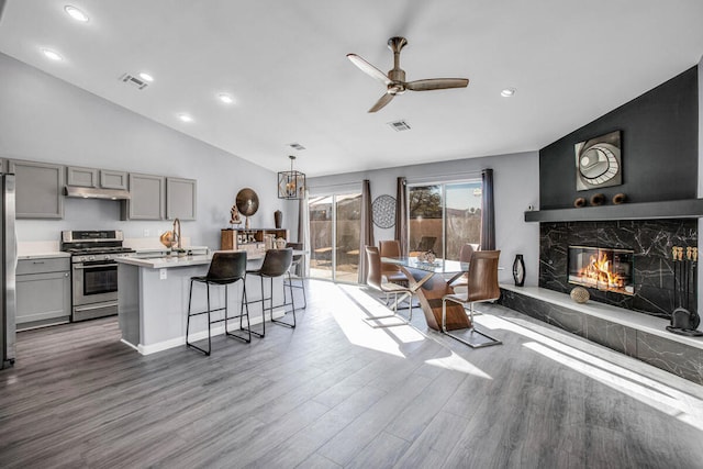 kitchen with hardwood / wood-style floors, a kitchen island with sink, gray cabinets, stainless steel appliances, and a fireplace