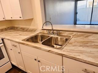 kitchen with sink, white cabinets, range, and light stone countertops