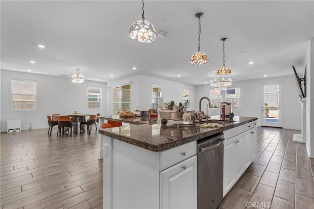 kitchen with decorative light fixtures, an island with sink, dishwasher, and white cabinets