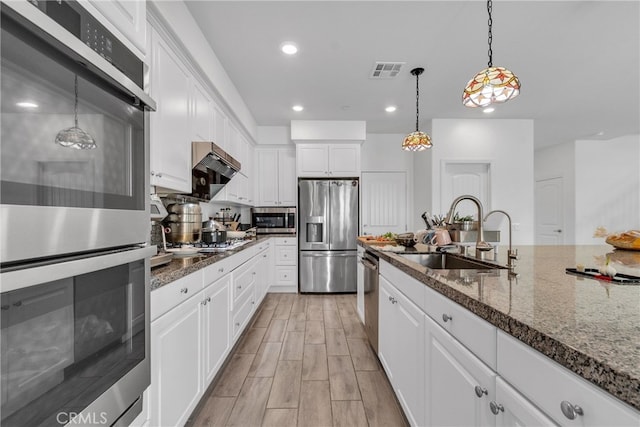 kitchen with stainless steel appliances, sink, white cabinetry, dark stone countertops, and hanging light fixtures