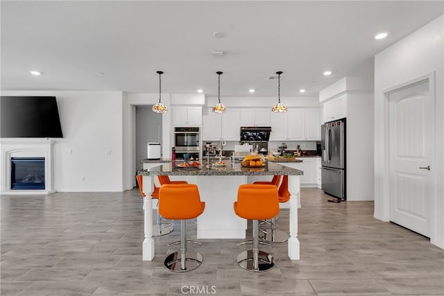 kitchen featuring stainless steel appliances, white cabinetry, a kitchen island with sink, and hanging light fixtures