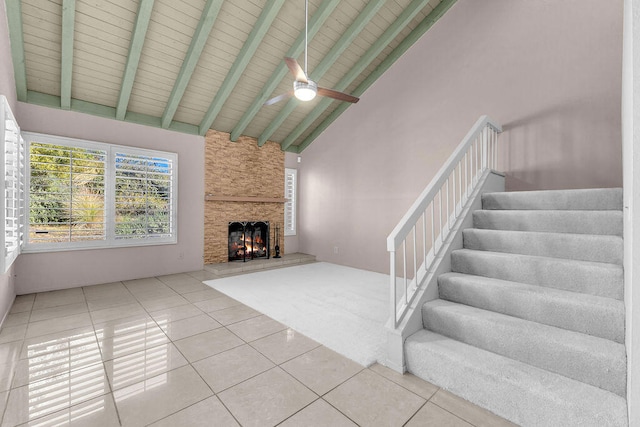 unfurnished living room featuring tile patterned flooring, a stone fireplace, high vaulted ceiling, ceiling fan, and beam ceiling