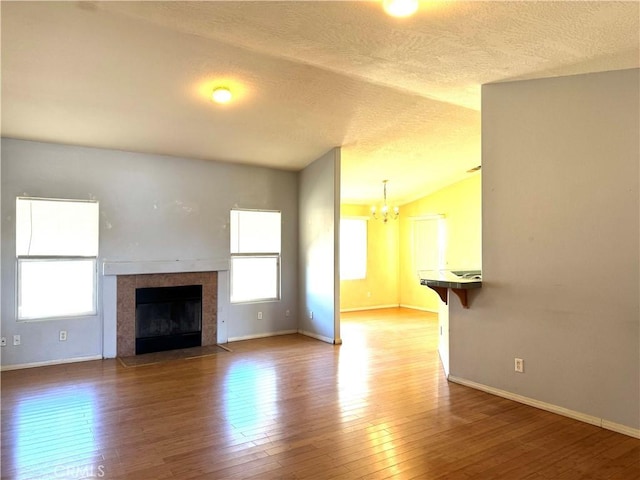 unfurnished living room with a textured ceiling, an inviting chandelier, vaulted ceiling, a tiled fireplace, and hardwood / wood-style floors