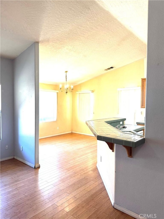 kitchen featuring an inviting chandelier, tile countertops, lofted ceiling, light wood-type flooring, and a breakfast bar