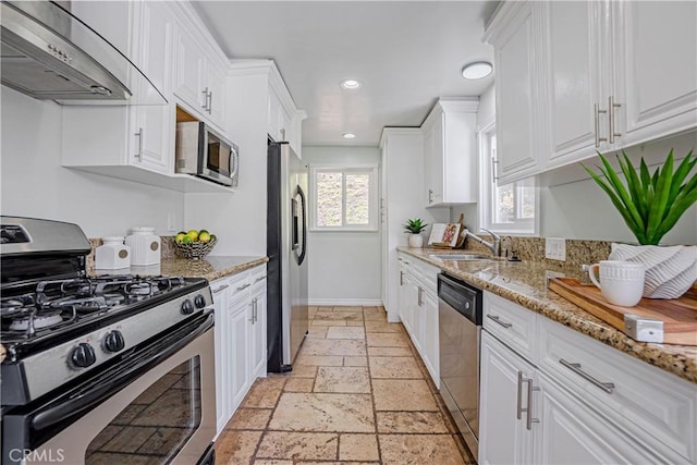 kitchen featuring stainless steel appliances, light stone countertops, wall chimney exhaust hood, white cabinets, and sink