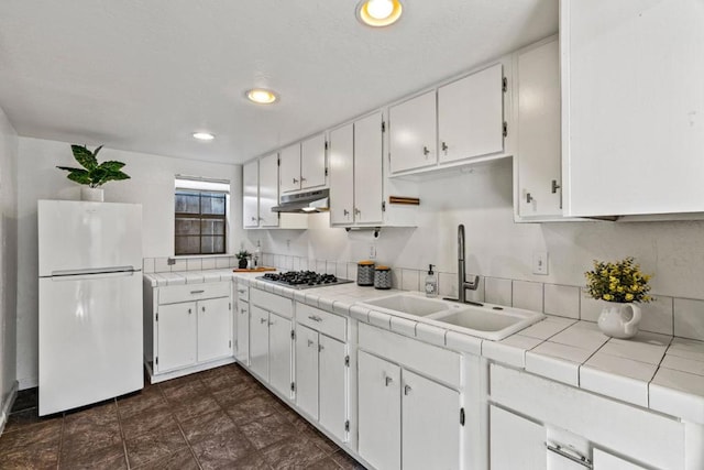 kitchen with white refrigerator, stainless steel gas stovetop, sink, and tile countertops