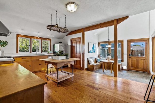 kitchen with light wood-type flooring, vaulted ceiling, stainless steel fridge, and sink