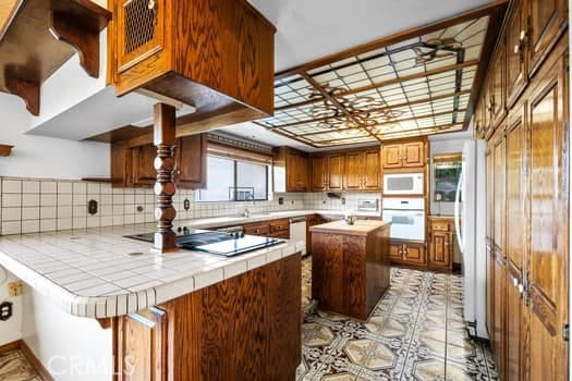 kitchen featuring tile countertops, white appliances, tasteful backsplash, kitchen peninsula, and plenty of natural light