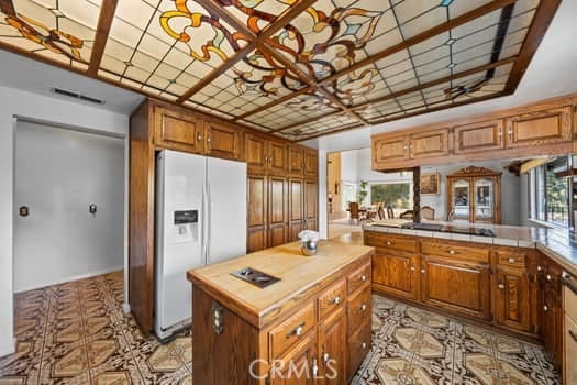 kitchen featuring a kitchen island, tile countertops, white fridge with ice dispenser, and kitchen peninsula