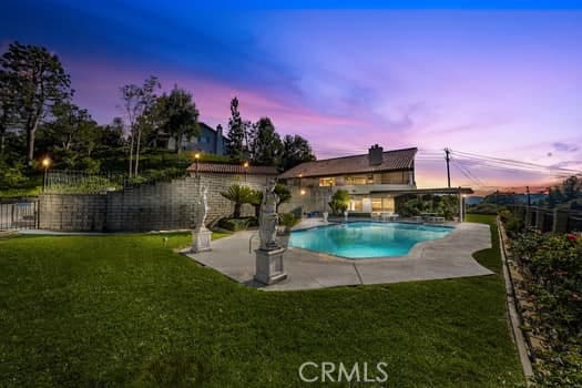 pool at dusk featuring a patio area and a lawn