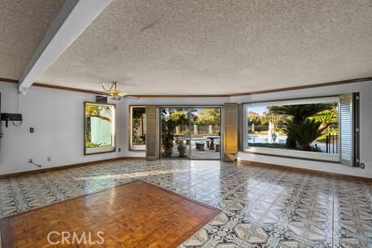 unfurnished living room with a textured ceiling, ceiling fan, crown molding, and beam ceiling