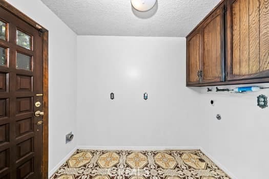 clothes washing area with electric dryer hookup, a textured ceiling, and cabinets