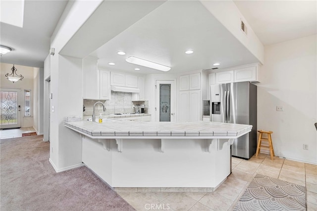 kitchen featuring kitchen peninsula, white cabinets, a breakfast bar area, and tile counters