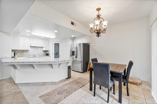 kitchen featuring white cabinets, tile counters, stainless steel fridge, kitchen peninsula, and light tile patterned floors