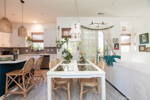 kitchen featuring white cabinetry, decorative light fixtures, stainless steel dishwasher, and a kitchen bar