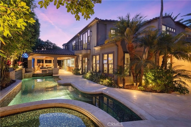 pool at dusk featuring a jacuzzi and a patio