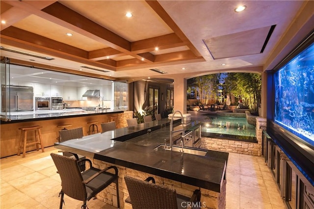 interior space with built in appliances, a tray ceiling, ventilation hood, beamed ceiling, and sink