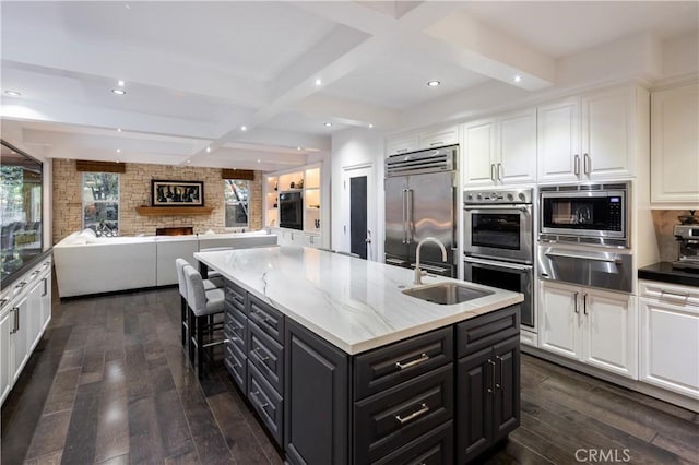 kitchen featuring sink, built in appliances, white cabinetry, dark hardwood / wood-style floors, and a center island with sink