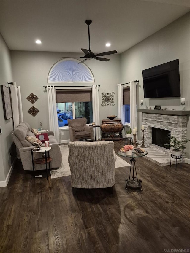 living room featuring ceiling fan, dark hardwood / wood-style flooring, and a stone fireplace