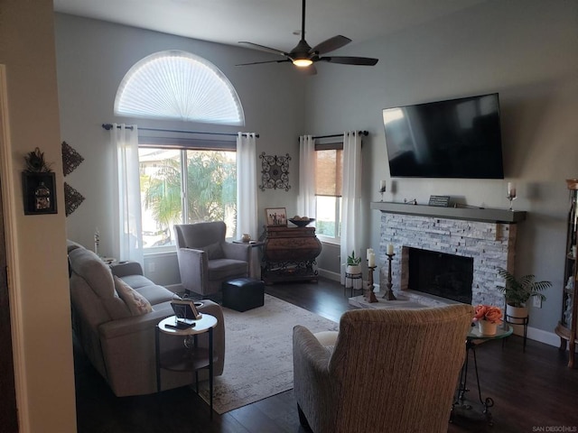 living room with ceiling fan, dark hardwood / wood-style flooring, a towering ceiling, and a stone fireplace