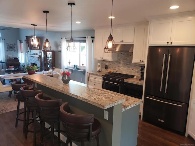 kitchen featuring high end refrigerator, hanging light fixtures, a breakfast bar area, black gas range oven, and white cabinets