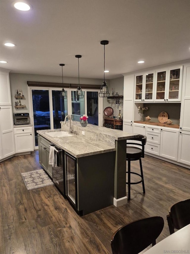 kitchen with dark wood-type flooring, decorative light fixtures, a center island with sink, and sink