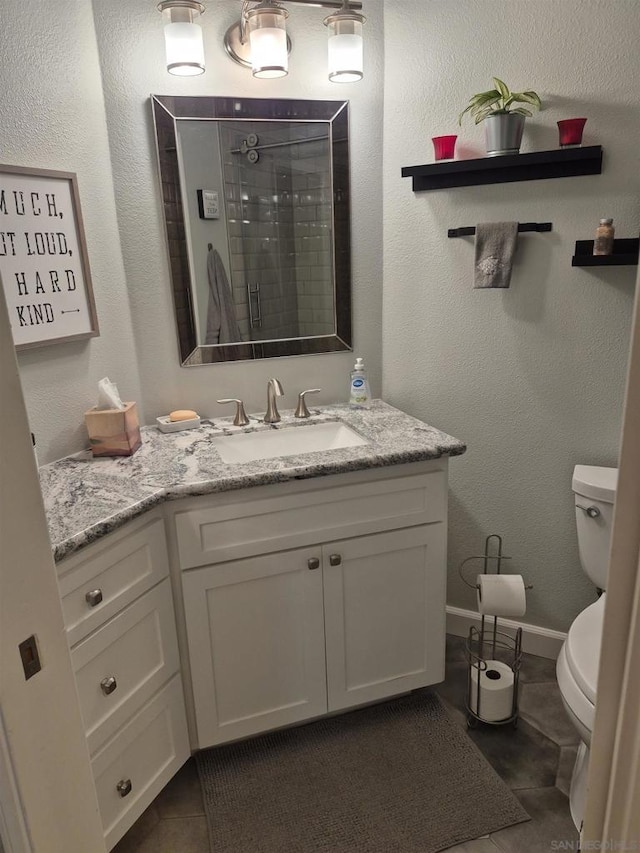 bathroom with toilet, vanity, tile patterned flooring, and tiled shower