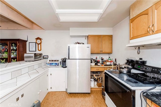 kitchen with fridge, range with electric stovetop, light hardwood / wood-style flooring, and tile counters