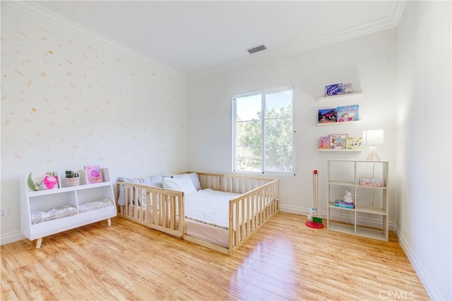 bedroom with hardwood / wood-style flooring, a nursery area, and ornamental molding