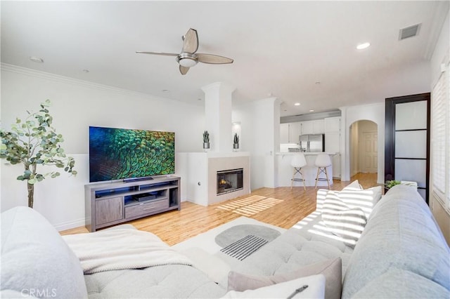 living room featuring ceiling fan, crown molding, and light hardwood / wood-style flooring