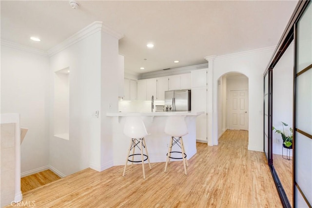 kitchen featuring light hardwood / wood-style floors, kitchen peninsula, white cabinetry, a kitchen breakfast bar, and stainless steel fridge