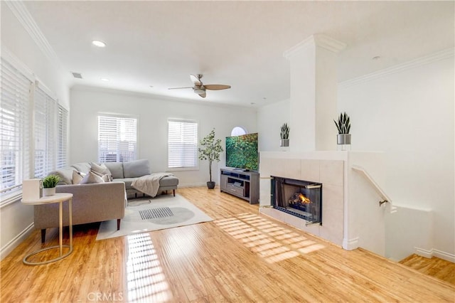 living room featuring ceiling fan, a tiled fireplace, crown molding, and hardwood / wood-style floors