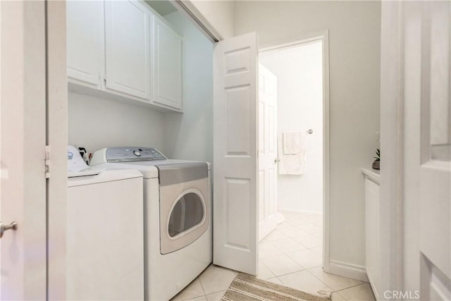 clothes washing area featuring washing machine and dryer, light tile patterned flooring, and cabinets