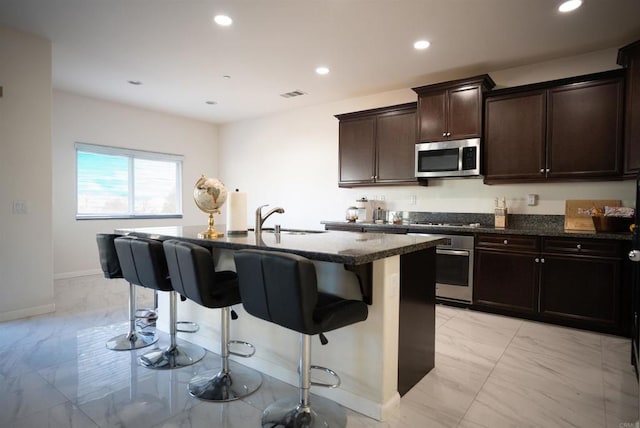 kitchen with stainless steel appliances, a center island with sink, sink, and a breakfast bar