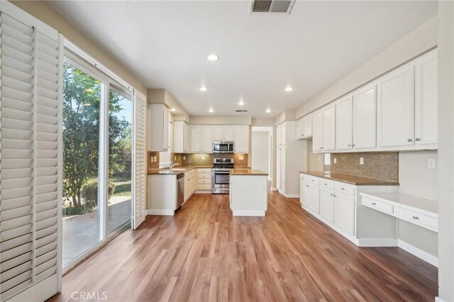 kitchen featuring light hardwood / wood-style floors, tasteful backsplash, a kitchen island, white cabinets, and appliances with stainless steel finishes