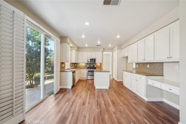 kitchen with light hardwood / wood-style flooring, white cabinetry, stainless steel appliances, built in desk, and a kitchen island