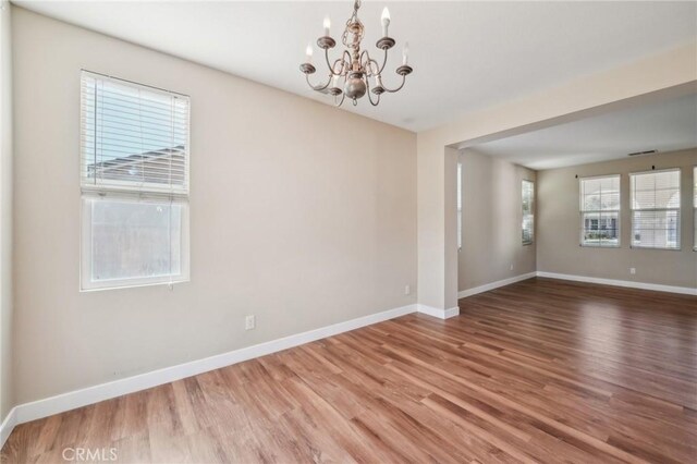 empty room featuring an inviting chandelier, hardwood / wood-style floors, and a healthy amount of sunlight