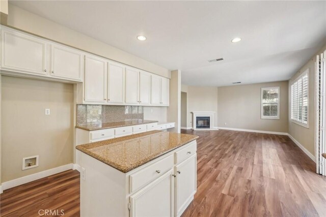 kitchen featuring light wood-type flooring, a center island, light stone counters, white cabinets, and backsplash