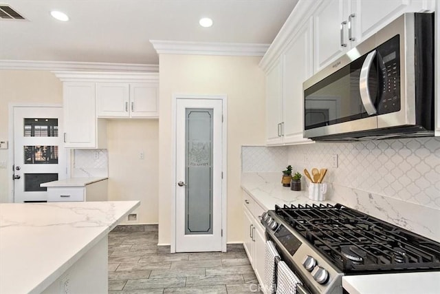 kitchen with white cabinetry, light stone counters, crown molding, and appliances with stainless steel finishes