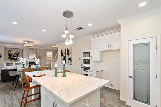 kitchen with decorative light fixtures, white cabinets, a center island, light stone counters, and ornamental molding