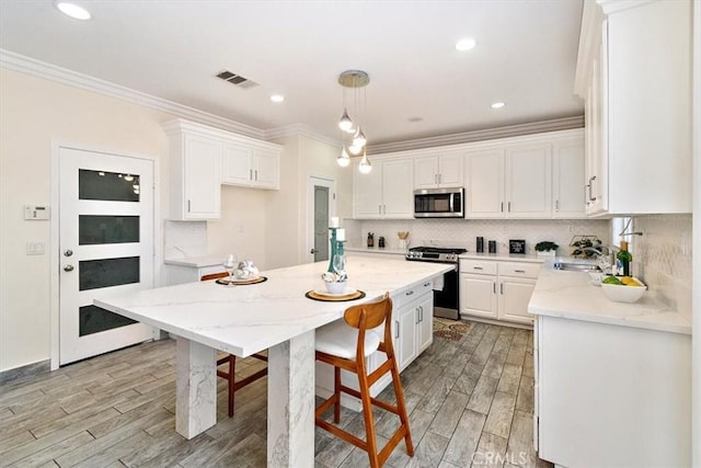 kitchen with appliances with stainless steel finishes, hanging light fixtures, light wood-type flooring, light stone countertops, and white cabinetry