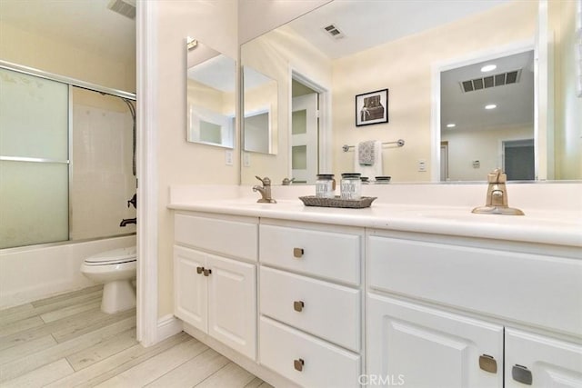 full bathroom featuring toilet, wood-type flooring, vanity, and bath / shower combo with glass door