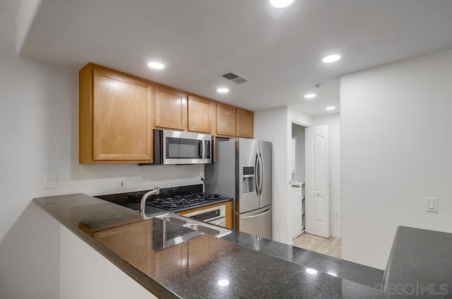 kitchen featuring dark stone counters, stainless steel appliances, sink, and kitchen peninsula