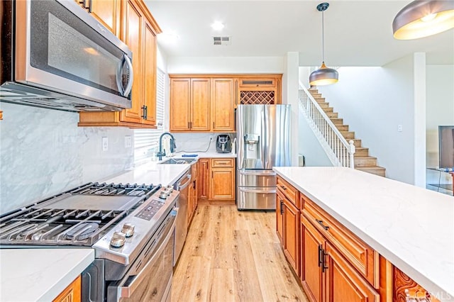 kitchen featuring sink, light hardwood / wood-style floors, decorative backsplash, pendant lighting, and appliances with stainless steel finishes