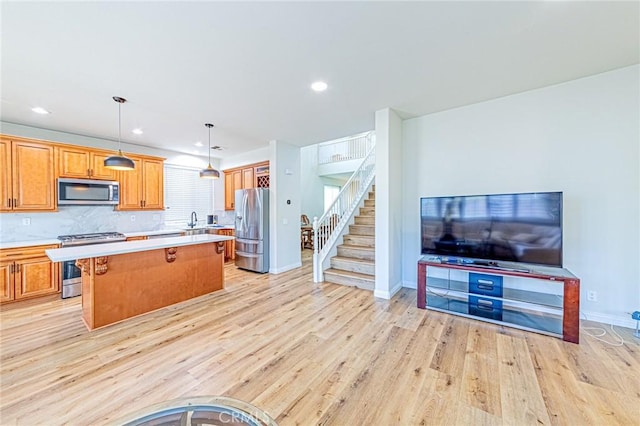 kitchen with light wood-type flooring, a breakfast bar area, backsplash, hanging light fixtures, and appliances with stainless steel finishes