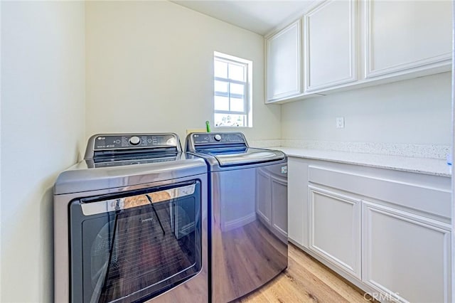 laundry area with cabinets, light wood-type flooring, and washing machine and clothes dryer