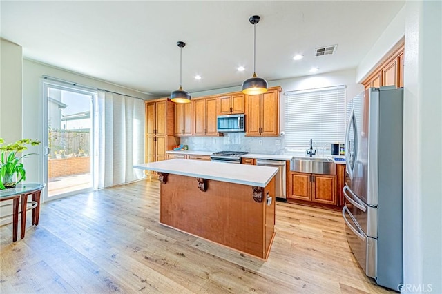 kitchen featuring appliances with stainless steel finishes, hanging light fixtures, light wood-type flooring, decorative backsplash, and a kitchen island